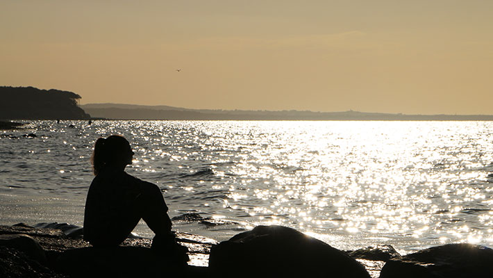 Frau beim Hypnose-Coaching, die am Strand am Meer sitzt und entspannt